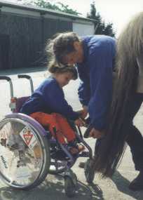 Margit hilft Kind im Rollstuhl Hufe auszukratzen